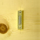 Close-up picture of one of the doorbell buttons in the experiment.
		This button has a small white rectangular plastic functional component. The casing is brass.